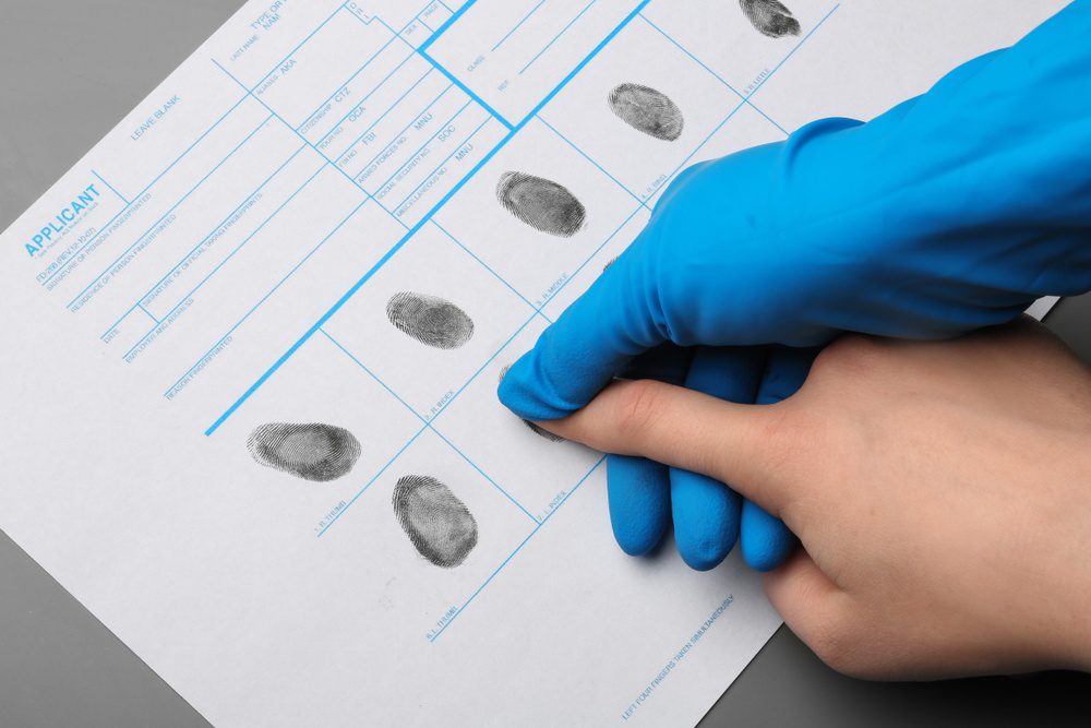A person in blue gloves helps an applicant put their fingerprints into a document.